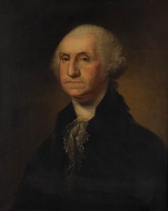 Color photograph of an oil painting of an older white man. He has receding white hair, most likely a powdered wig, pulled back and tied with a ribbon at the nape of his neck, and dark eyes. He wears a detailed filmy white lace cravat and a dark or black jacket with a high collar. He sits in a three-quarter profile view to the left but looks at the viewer. The background is plain browns with a highlight of light sitting directly behind the sitter’s neck getting concentrically darker as it goes towards the edges.