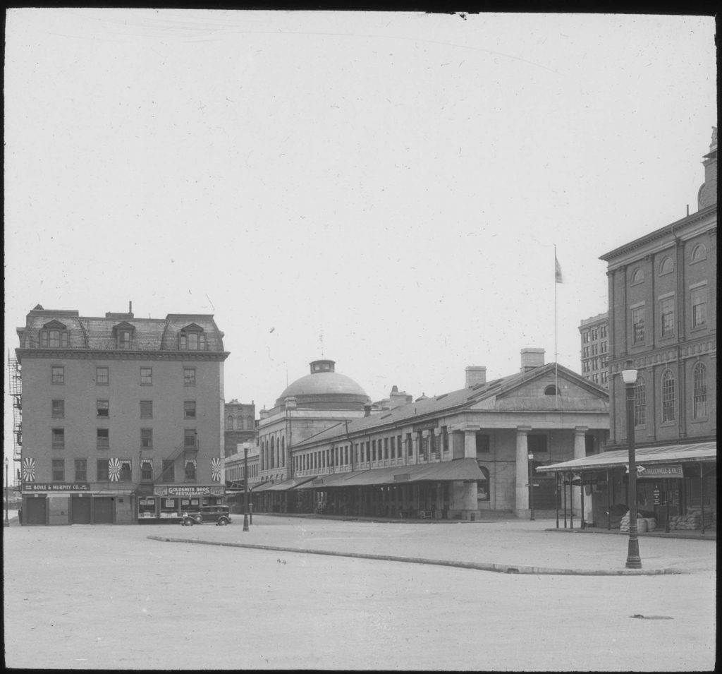 Black and white photograph of several buildings with Quincy Market the central focus and a large empty square in the foreground. 