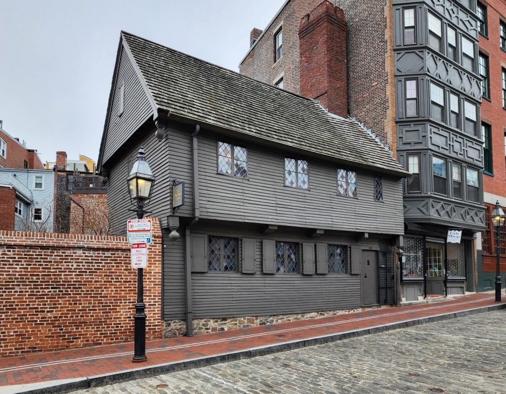 The wooden, two story house of Paul Revere stands out between taller, modern buildings.