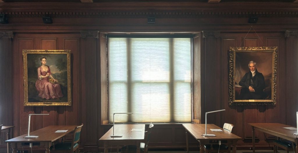 The walls of Ellis Hall, which are symmetrically organized with paintings, pilasters, and windows. Tables for research sit in the foreground.