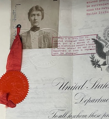 Close up color photograph of a passport. In the upper left is the black and white photograph of a young white woman wearing a white shirt and light-colored dress looking directly at the viewer. Attached to the image is a ribbon that is held down by a red wax seal below the photograph. To the right is red stamped words in a red box and the left part of the US Eagle, underneath which are the words "United State...Departme..." 