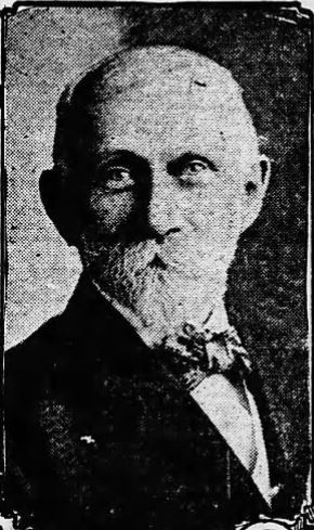 Black and white photograph of a white man with short gray hair, a mustache, and a beard wearing a black suit and a bowtie.