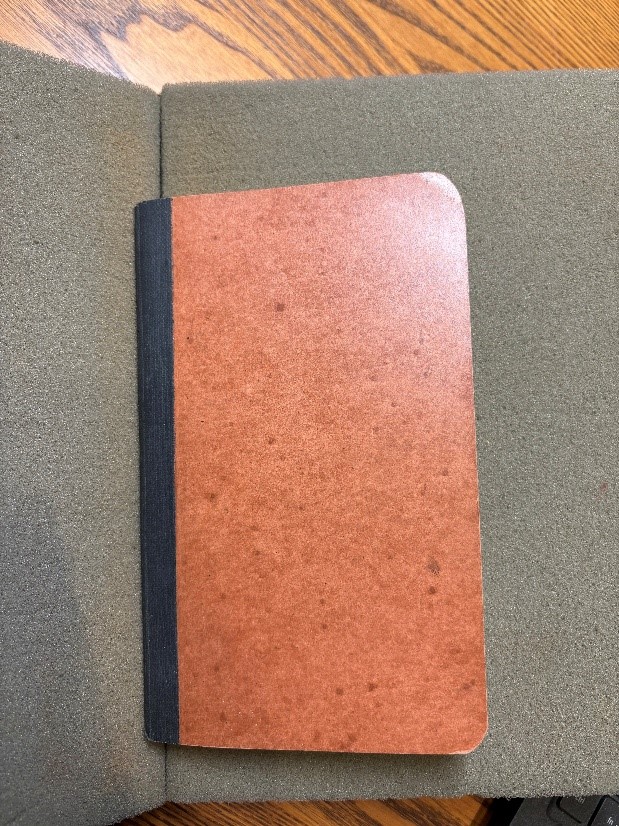 The front cover of a small, brown paperbound diary on top of a bookrest in the MHS reading room.