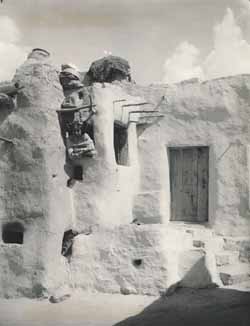 Unidentified woman leaning through window of adobe building Platinotype photograph