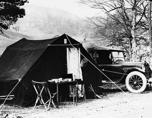 A car and tent, with a table set up for food Lantern slide