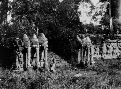 A man standing outside of an overgrown structure, Southeast Asia Lantern slide