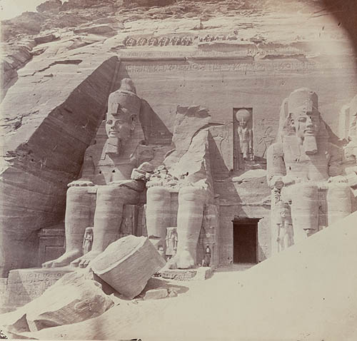 View of Abu Simbel including a man (a dragoman) standing next to the feet of one colossus of Ramses II Photograph